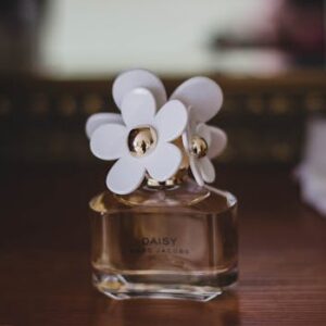 Close-up of a Marc Jacobs Daisy perfume bottle with flower caps on a wooden table.