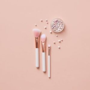 Flat lay of makeup brushes and pearlescent powder balls on a beige background. Ideal for beauty and cosmetic themes.